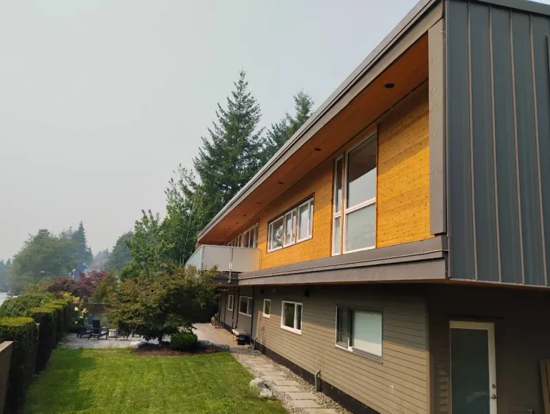 After: Rear elevation of house showing siding upper level, lower level siding, windows, balcony railing, and yard, . Arbour woods, Squamish, BC