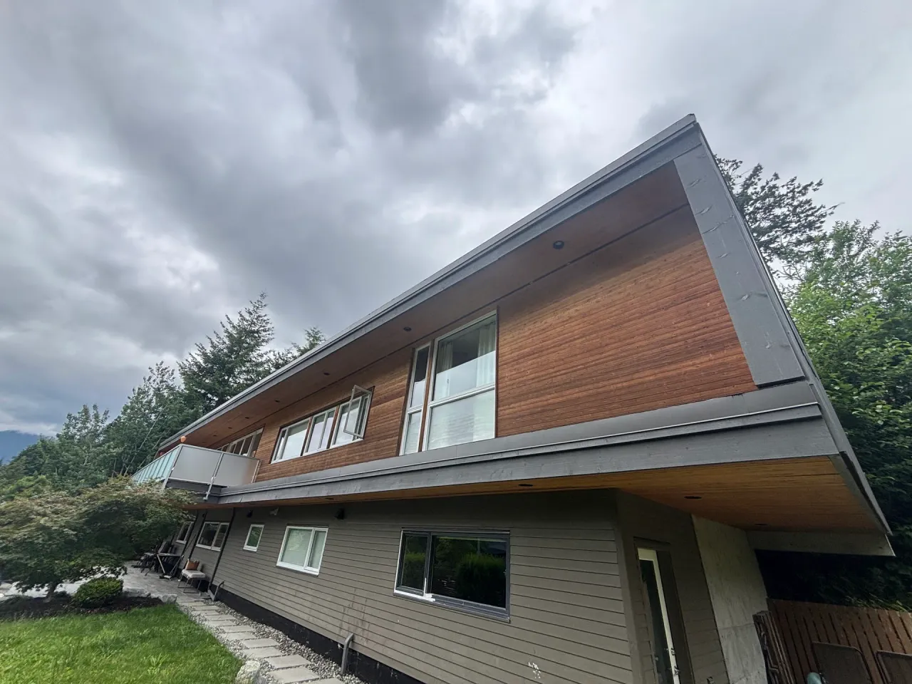 Before: Rear elevation of home showing upper siding gable, windows, and lower level siding above a patio, . Arbour woods, Squamish, BC
