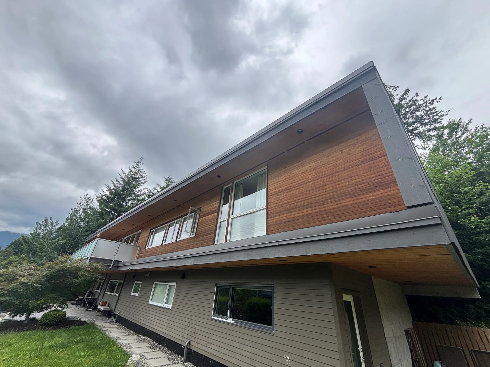 Before: Rear elevation of home showing upper siding gable, windows, and lower level siding above a patio, . Arbour woods, Squamish, BC