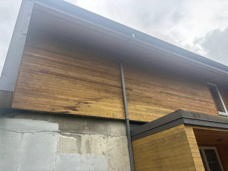 Before: Upward view of eave and siding soffit on the side of the house above a concrete foundation, . Arbour woods, Squamish, BC