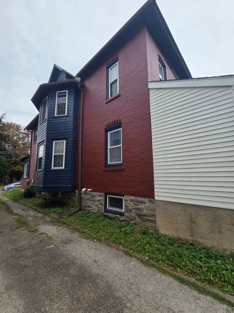 After: Side elevation of a house with a repainted bay window section in dark blue and the main wall in deep red, next to a light-colored addition., Ardmore Lower Merion, PA
