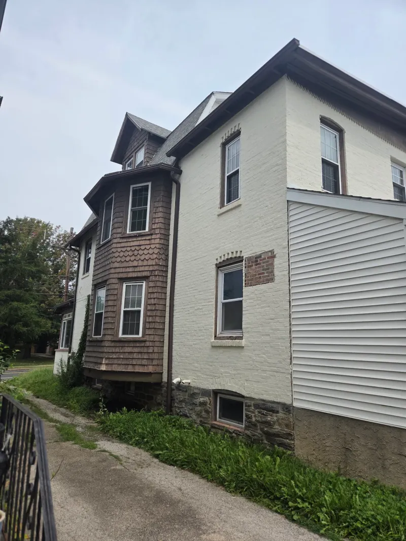 Before: Side elevation of a house with a projecting bay window section, painted trim, and an adjoining addition with lighter siding., Ardmore Lower Merion, PA