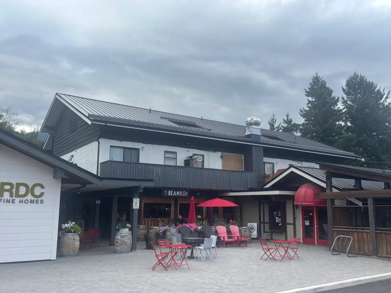 After: Wide front elevation of a building with dark roof, white walls, black trim and siding, and a ground-floor cafe entrance, Brackendale, Squamish, BC