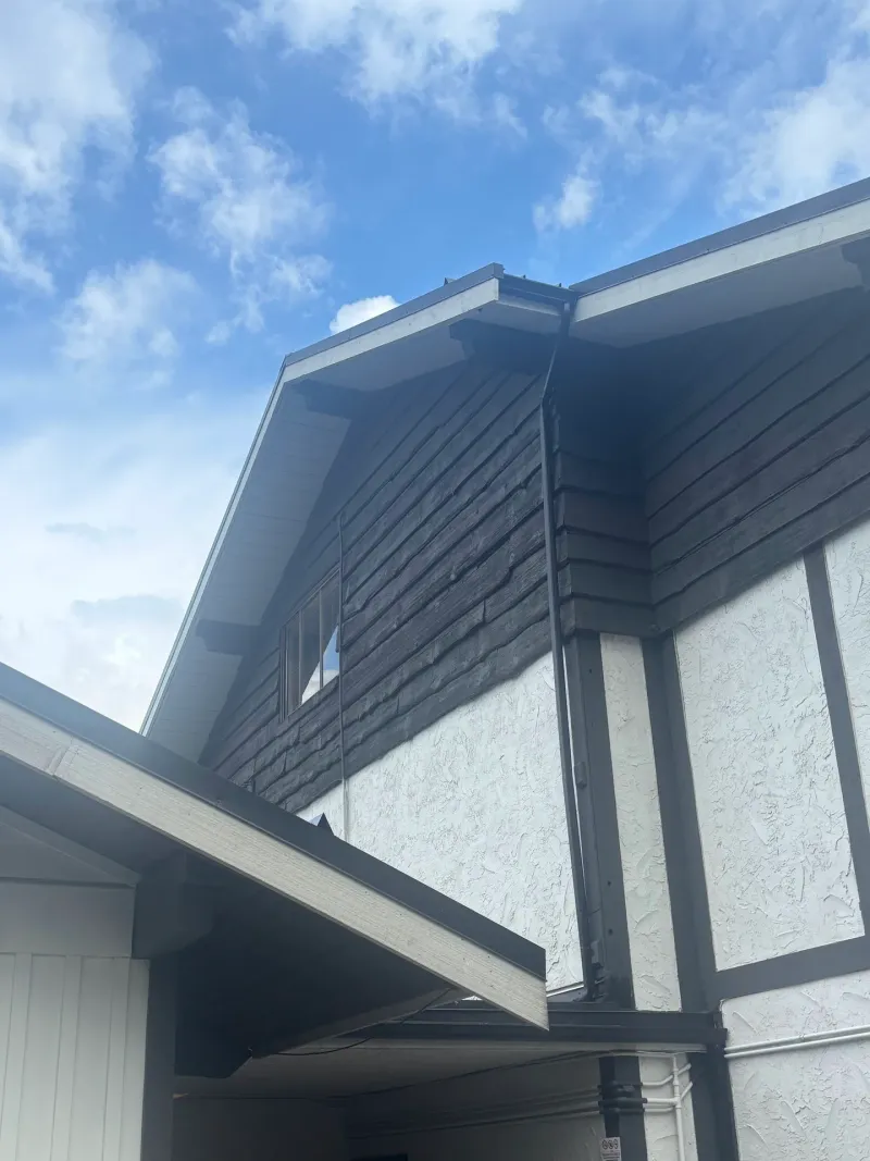 After: Gable and eave of a building showing dark siding over white wall under a blue sky, Brackendale, Squamish, BC