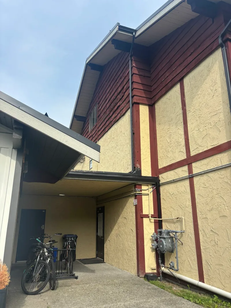 Before: Side elevation corner showing siding over wall with a gas meter and covered walkway, Brackendale, Squamish, BC