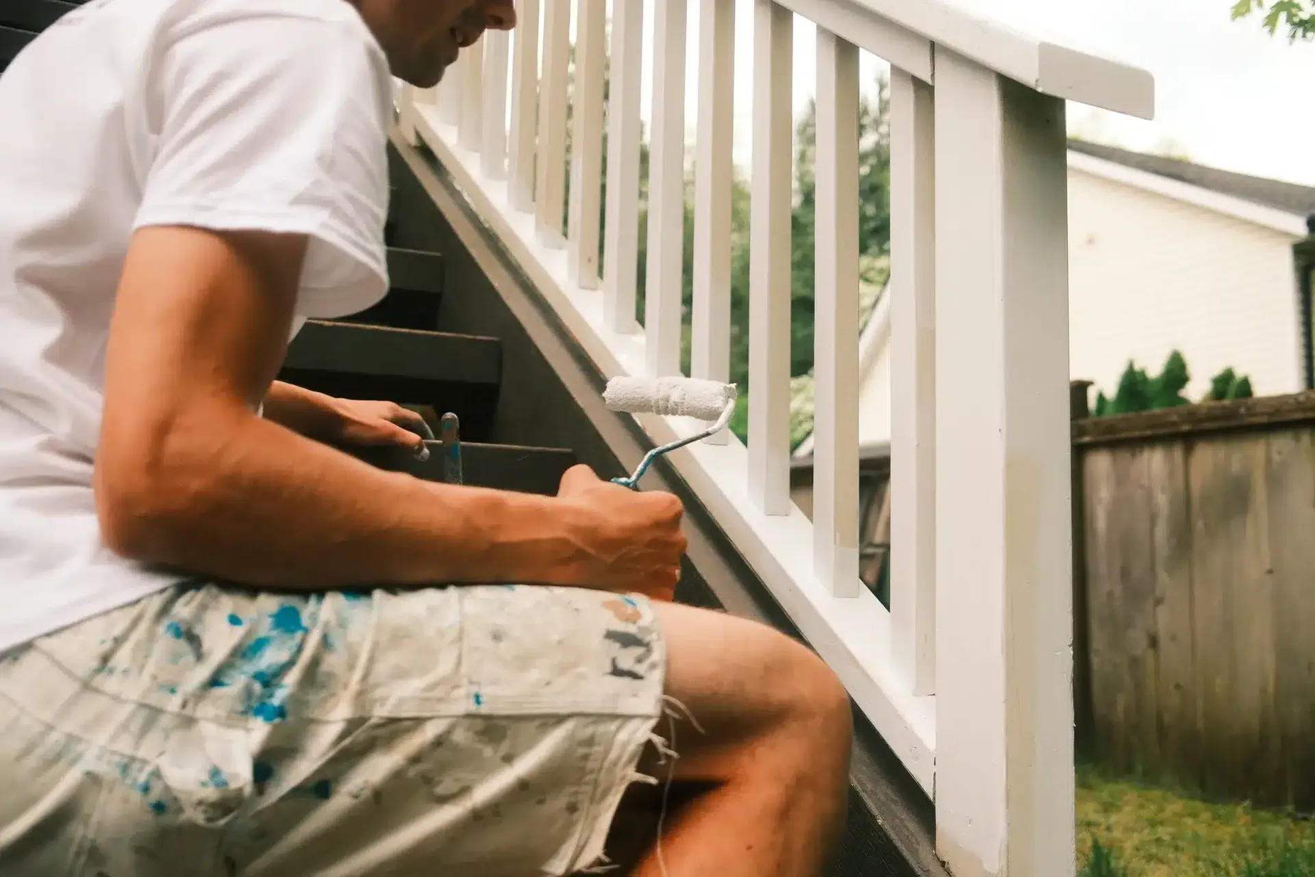 Painter using roller to paint white balusters on outdoor staircase, deck painting by Colour Craft Painting