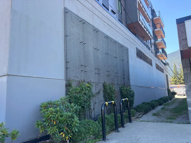 Before: Side elevation of building wall with protective screen and bike racks along walkway, Downtown, Squamish, BC
