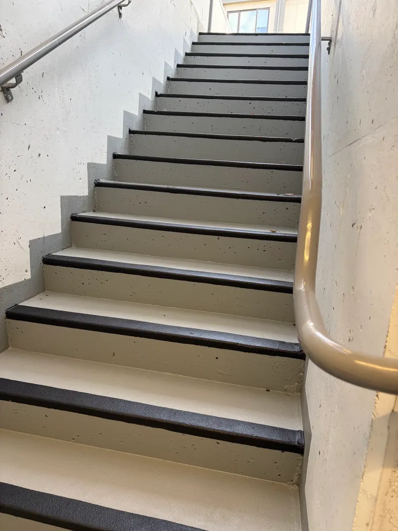 After: Concrete stairwell viewed from the bottom looking up at freshly painted stair treads and handrail, Downtown, Squamish, BC