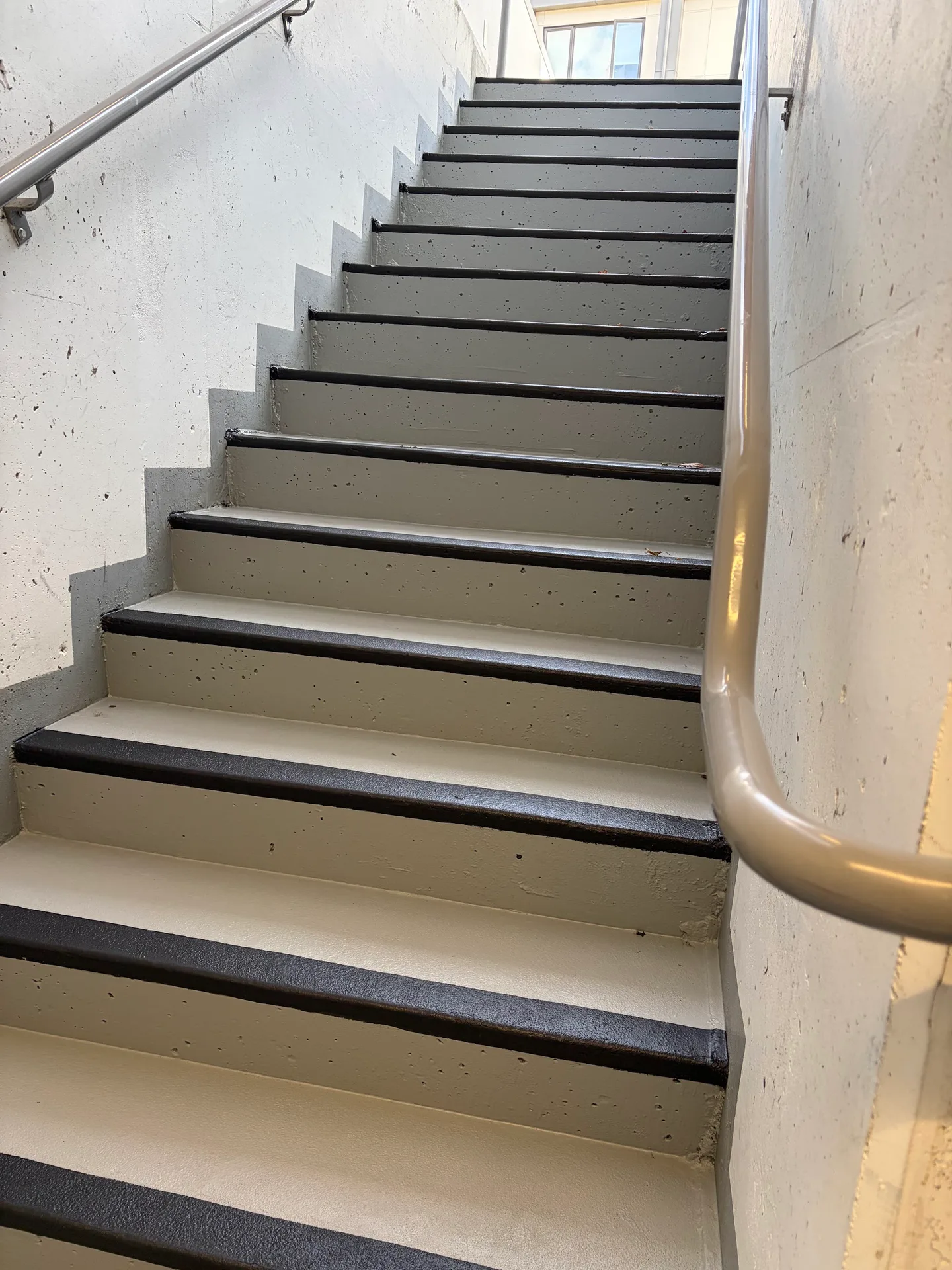 After: Concrete stairwell viewed from the bottom looking up at freshly painted stair treads and handrail, Downtown, Squamish, BC