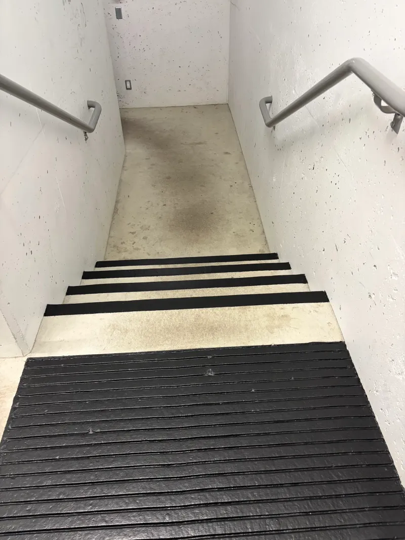 After: Stairwell with new dark nonslip stair treads descending toward a concrete landing, Downtown, Squamish, BC