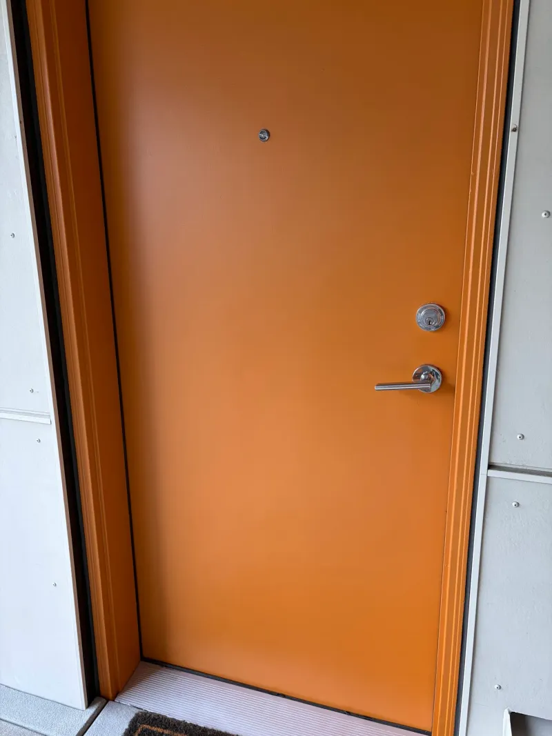 After: Close view of a freshly painted orange entry door with modern lever handle and deadbolt, Downtown, Squamish, BC