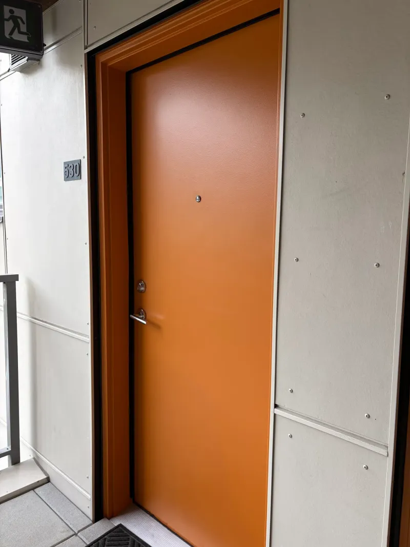 After: Orange entry door opened at an angle beside painted wall panels and a railing, Downtown, Squamish, BC