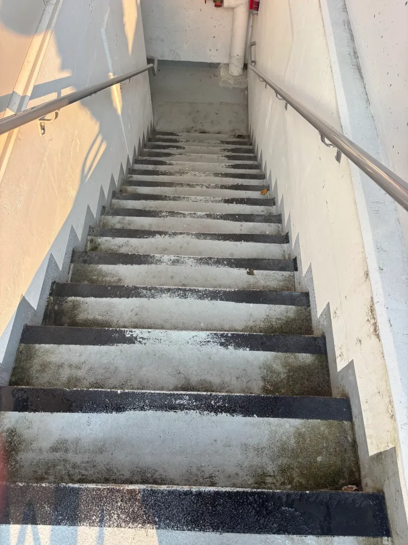 Before: Interior concrete stairwell with worn, stained stair treads and metal handrails on both sides, Downtown, Squamish, BC