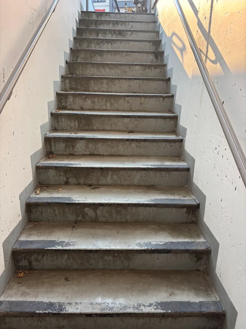 Before: Concrete stairwell viewed from the bottom looking up at worn stair treads and side walls, Downtown, Squamish, BC