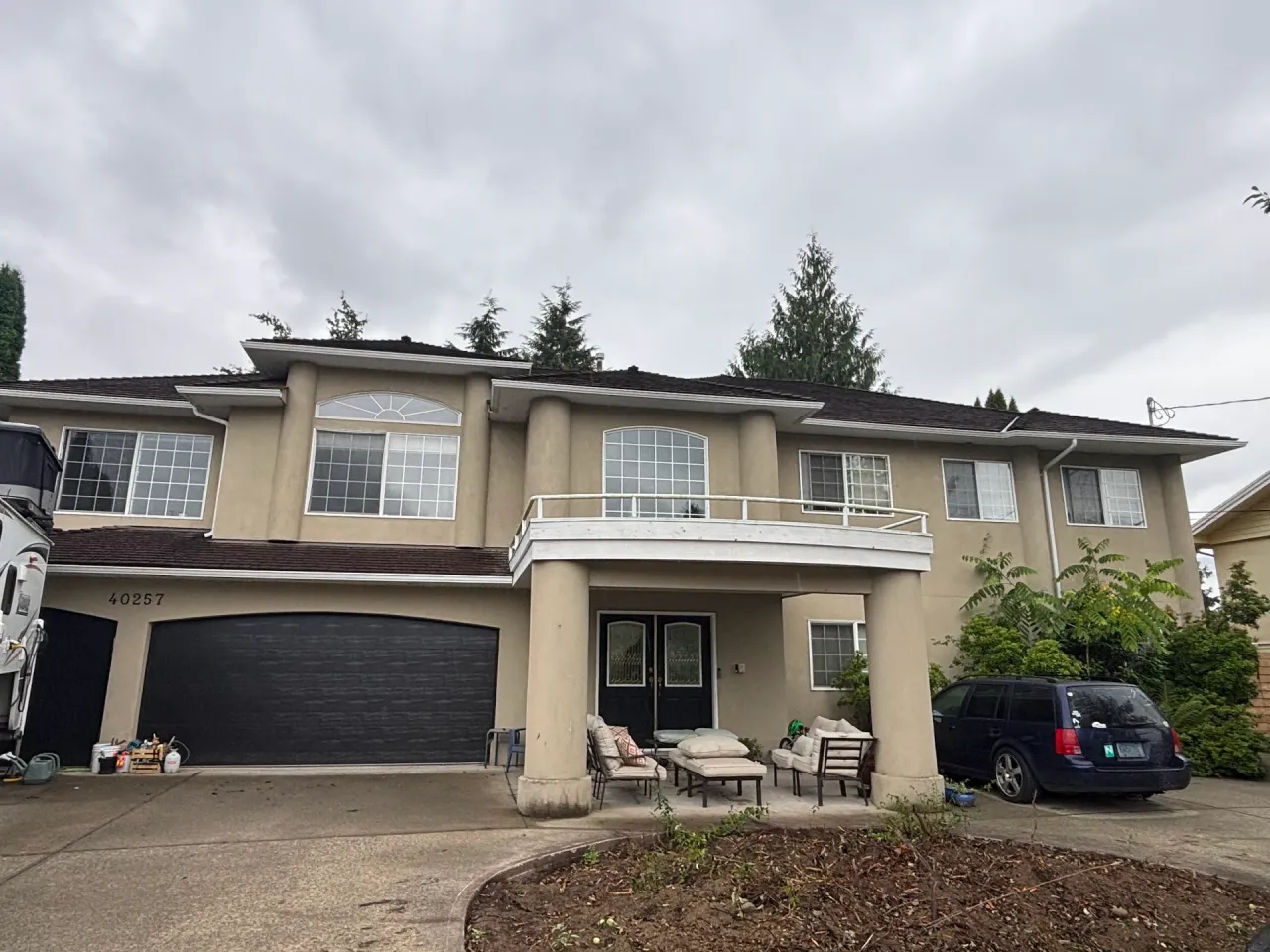 Before: Front elevation of a two-story house with a curved upper balcony, covered entry porch, and attached double garage, Garibaldi highlands, Squamish, BC