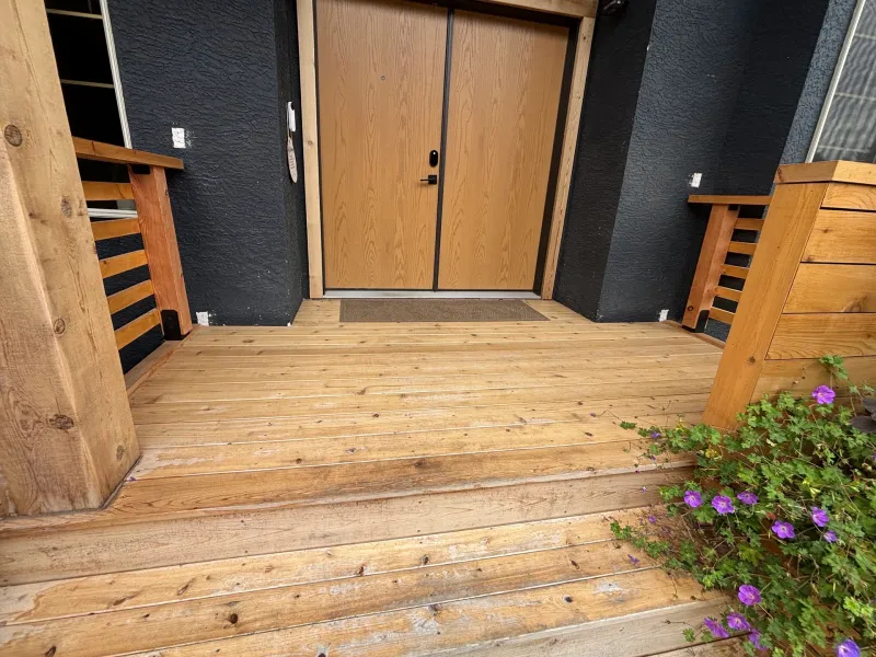 Before: Front entry door and deck landing with side railings and a planter with flowering plants, Highlands, Squamish, BC