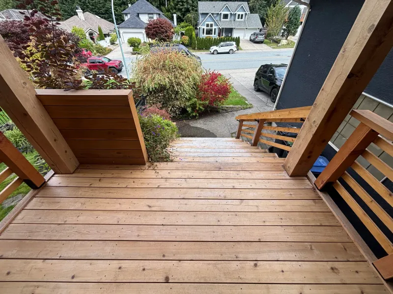 Before: View down the front deck and staircase toward the street, showing unpainted decking and railings, Highlands, Squamish, BC