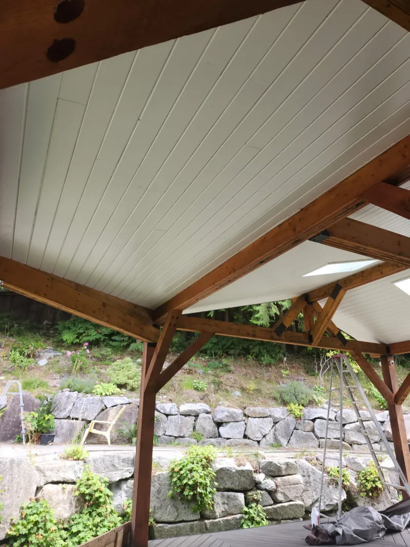 After: Painted white patio ceiling with exposed beams above a stone retaining wall, - Isabella Rd, Salt Spring Island, BC