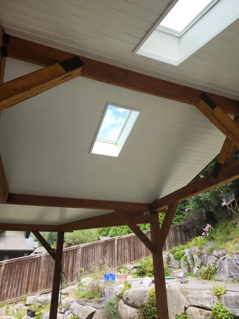 After: Painted white patio ceiling with beams and skylights above a fenced backyard, - Isabella Rd, Salt Spring Island, BC