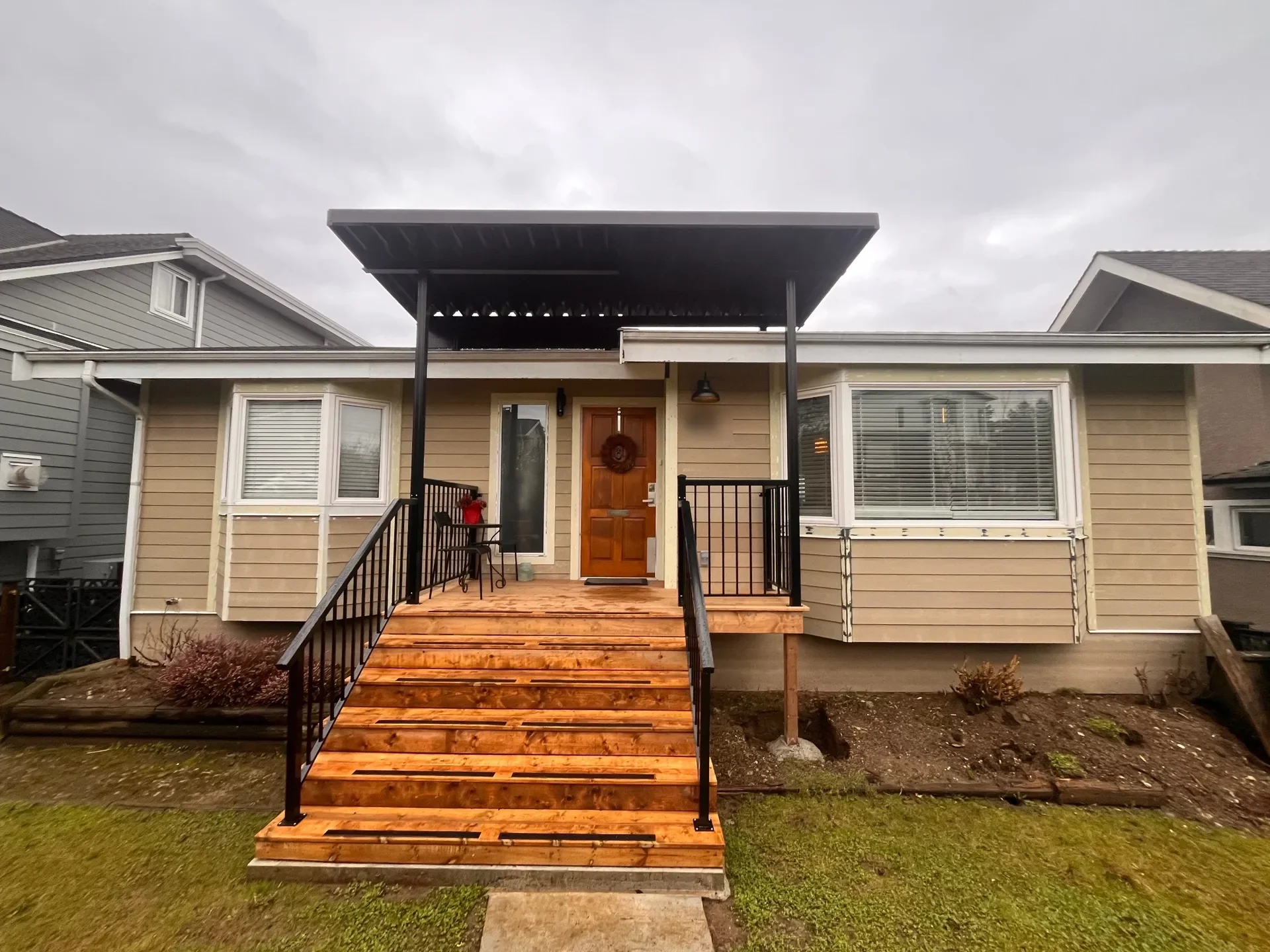 Before: Front elevation of house with covered entry porch, steps, black railings, and door, New Westminster, BC