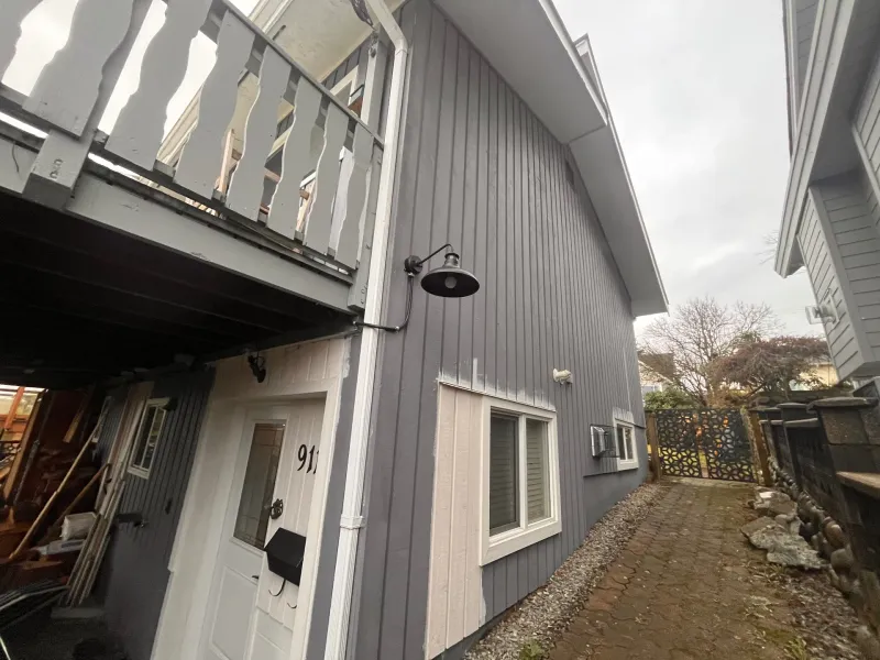 Before: Side elevation of house with vertical siding, upper balcony railing, and windows, New Westminster, BC