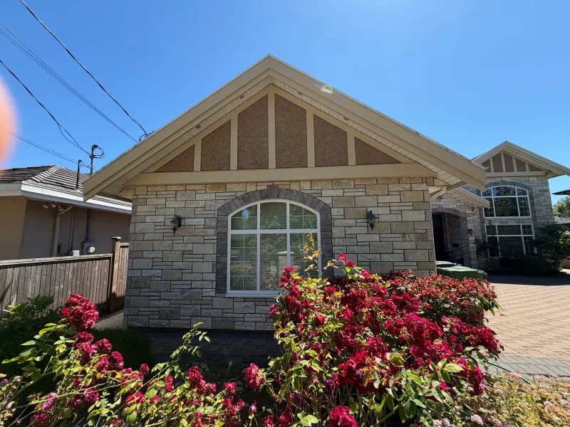 After: Front gable section of house with stone wall, arched window and flowering shrubs, Seafair, Richmond, BC