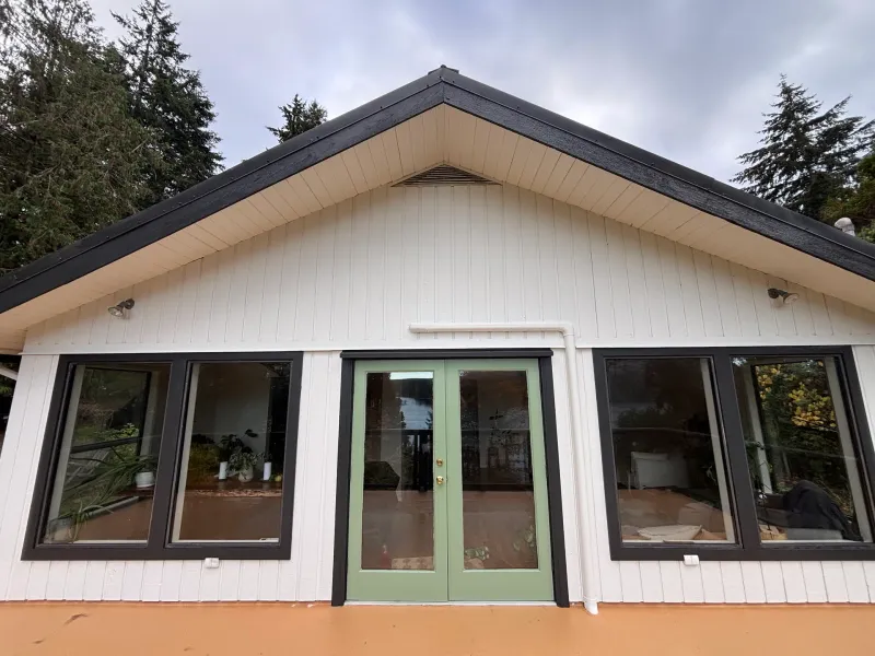 After: Gable end of house with cream siding, dark trim, large windows, and green french doors, Souther Salt Spring. Isabella Point / Roland Rd, BC