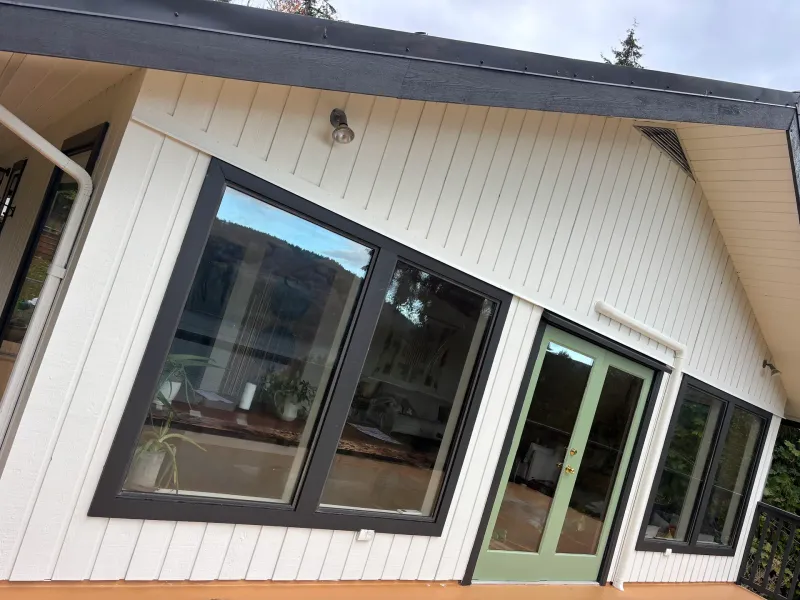 After: Corner of house with cream siding, dark trim, large window, and green door, Souther Salt Spring. Isabella Point / Roland Rd, BC