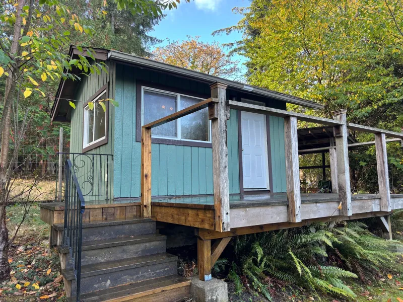 Before: Side view of small teal cabin with white door, window, deck, and stairs, Souther Salt Spring. Isabella Point / Roland Rd, BC