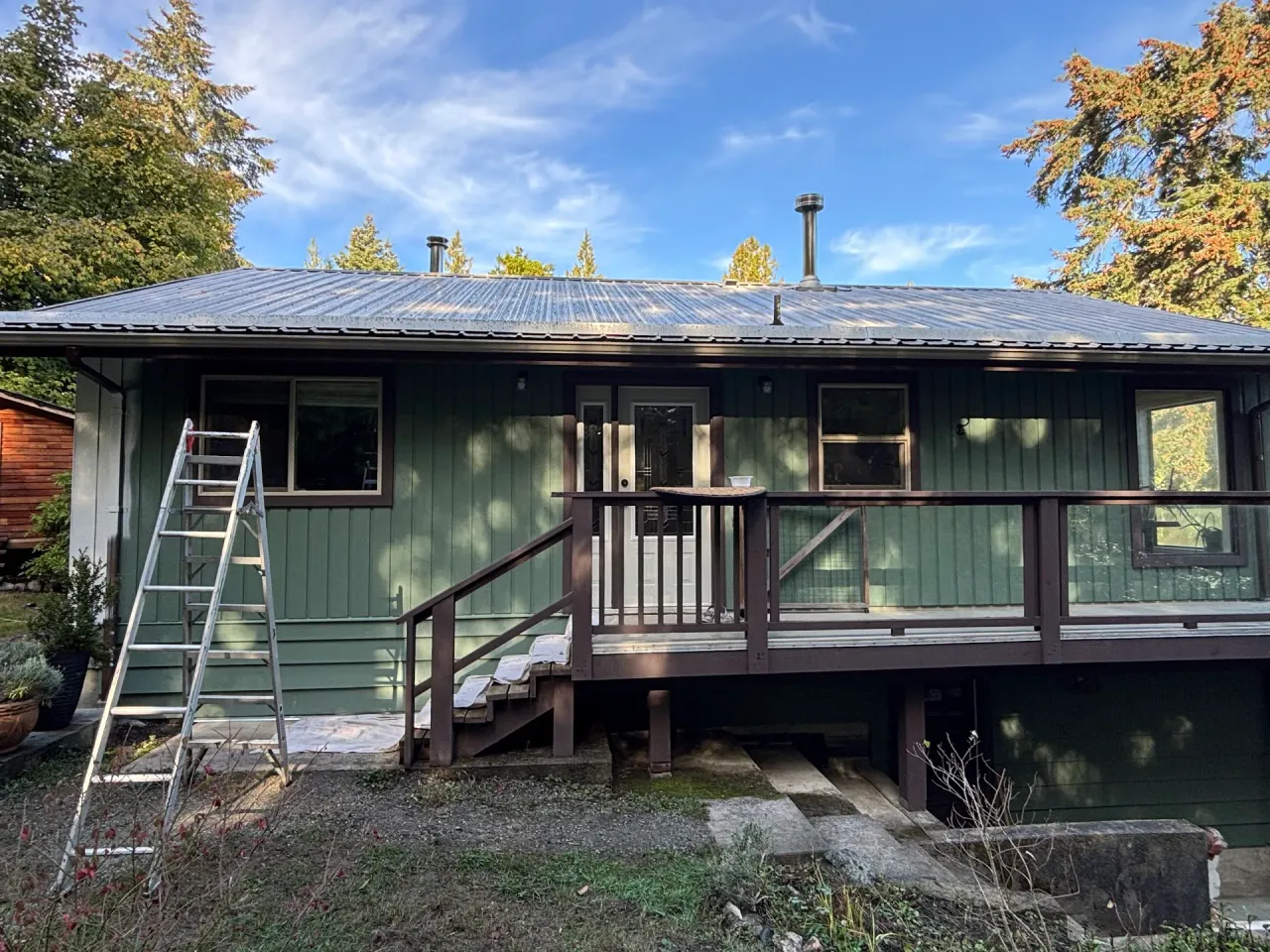 Before: Rear elevation of house with green vertical siding, metal roof, deck, and railing, Souther Salt Spring. Isabella Point / Roland Rd, BC