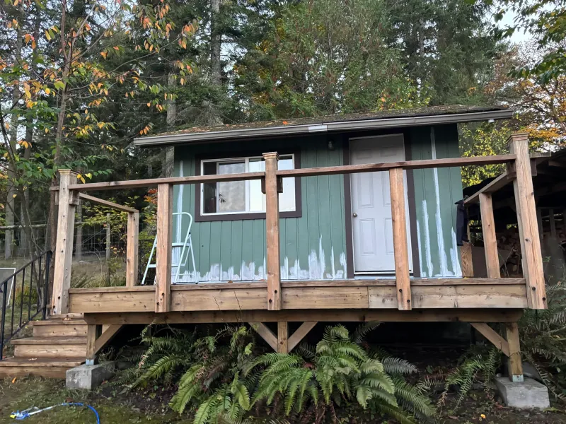 Before: Rear elevation of small cabin with window, door, and partially painted siding, Souther Salt Spring. Isabella Point / Roland Rd, BC