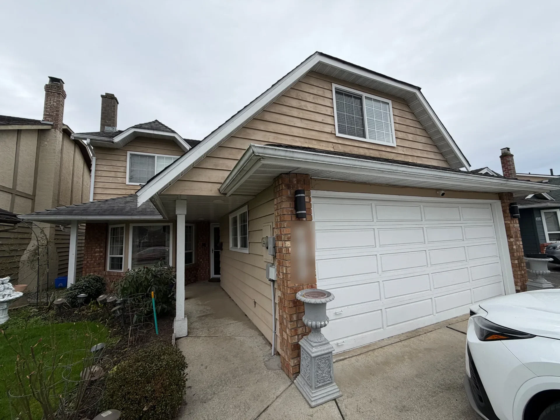 Before: Front elevation of two-story house with double garage door, columns, and upper window gable, Steveston, Richmond, BC