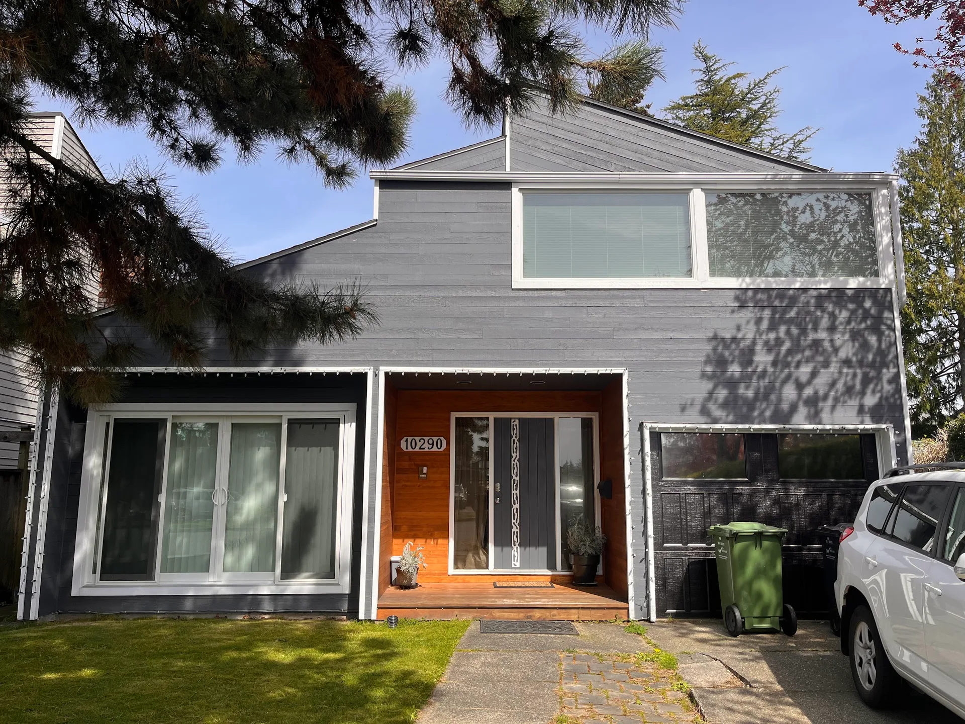 Before: Front elevation of two-story house with gray siding, white trim windows, toned entry alcove and dark garage door, Steveston, Richmond, BC
