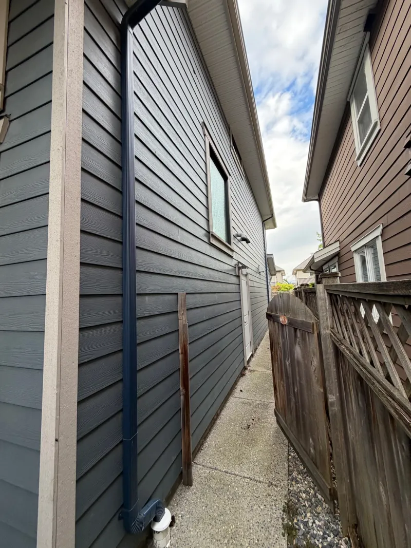 Before: Side elevation of house with siding, trim, window, and rear door along narrow walkway, Steveston, Richmond, BC