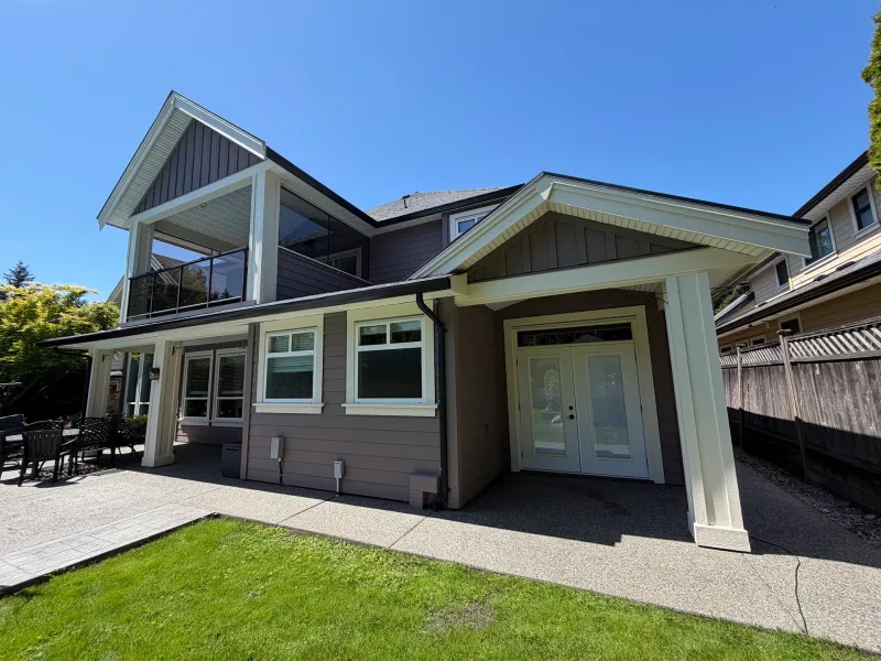 After: Rear of two-story house with upper balcony, covered patio, French doors, and multiple windows, Tsawwassen, Delta, BC
