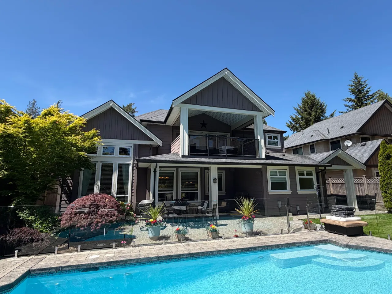 After: Rear of two-story house with balcony, covered patio, and landscaped yard overlooking a pool, Tsawwassen, Delta, BC