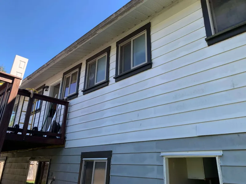 Before: Side of house with upper and lower windows, dark trim, and siding needing paint, deck to the left, - Valley Cliff, Squamish, BC