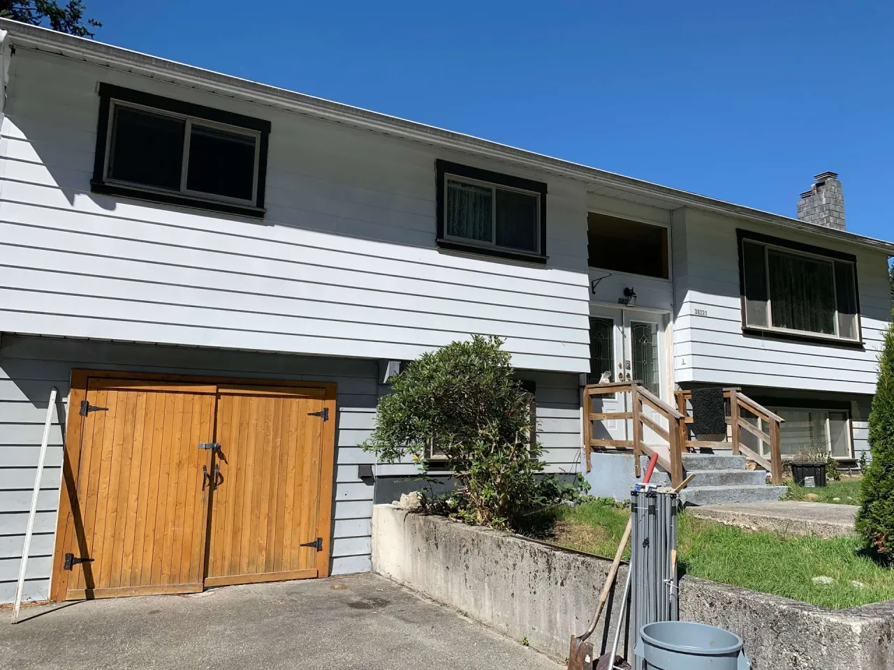 Before: Front of house with garage door, entry stairs, and siding needing paint, - Valley Cliff, Squamish, BC
