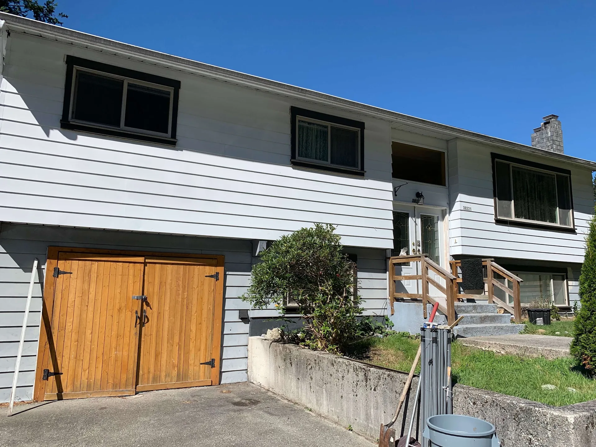 Before: Front of house with garage door, entry stairs, and siding needing paint, - Valley Cliff, Squamish, BC
