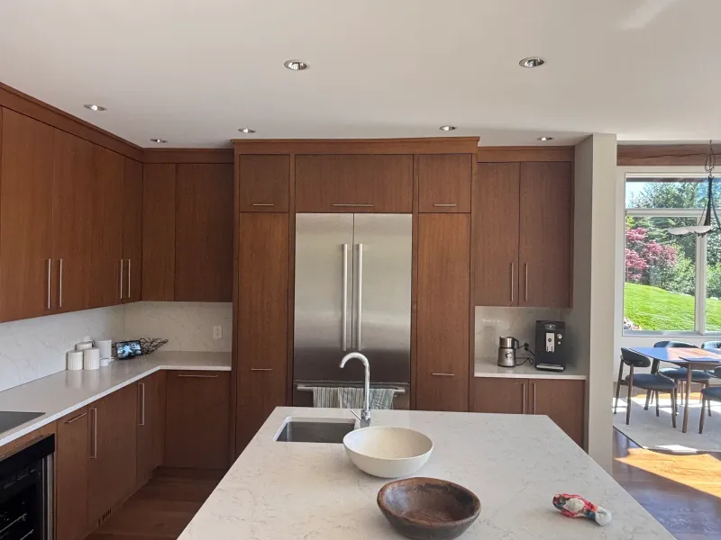 Before: Kitchen with tall cabinets flanking a stainless refrigerator, island countertop, and dining area beyond, Whistler, BC