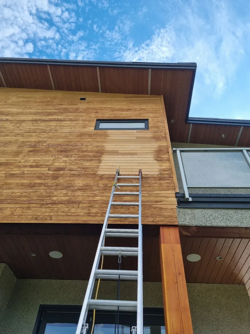 Before: Upward view of siding and fascia on upper corner of house with a narrow window, Whistler, BC