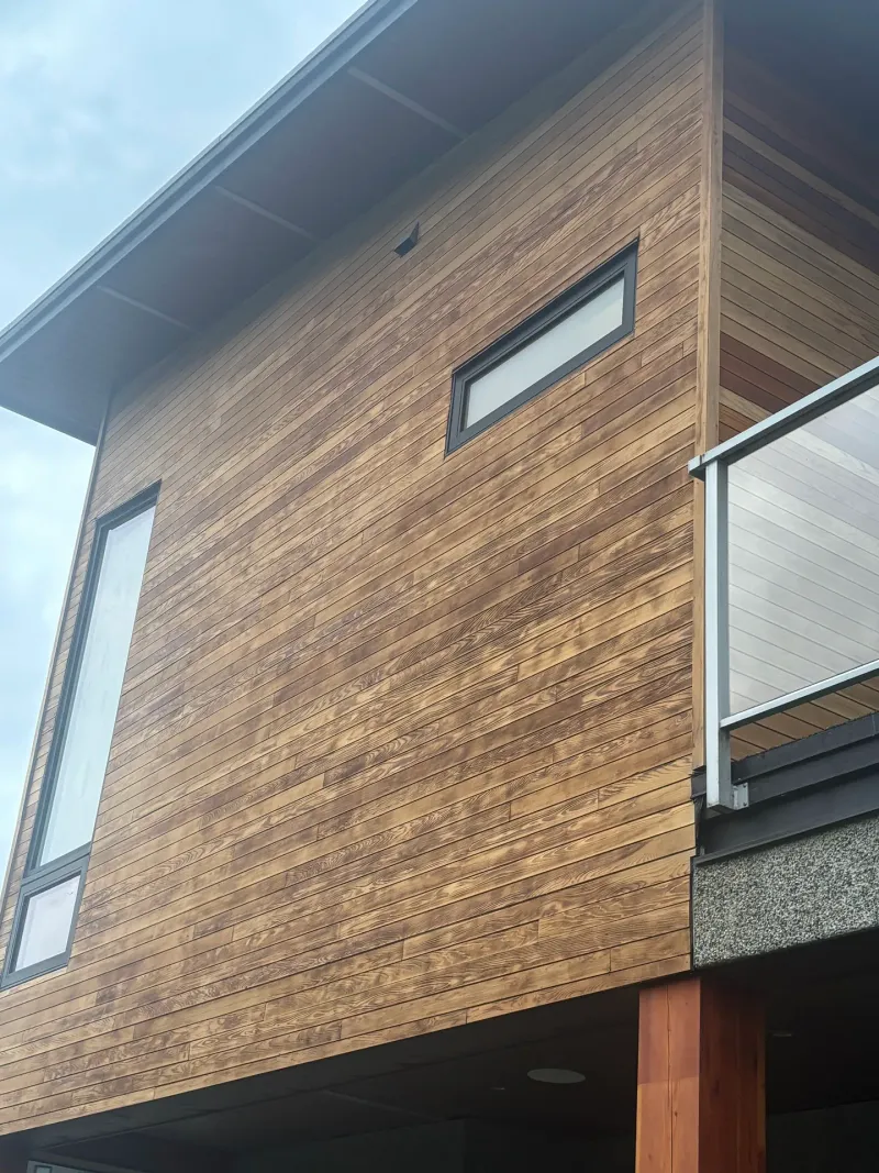 Before: Upward view of siding corner elevation with two narrow windows and a glass railing, Whistler, BC