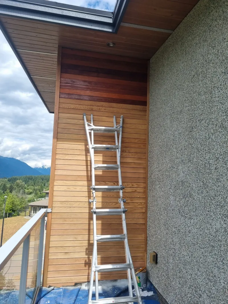 Before: Balcony side wall with siding and ladder leaning against it, mountain view behind, Whistler, BC