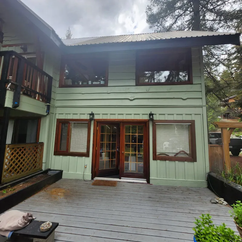 After: Rear elevation of house with green siding, French doors, and upper windows after painting, Whistler, BC