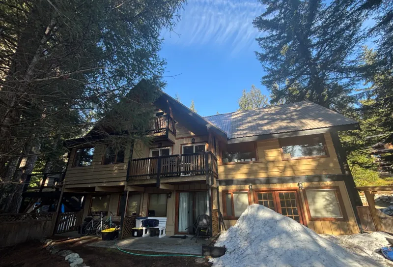 Before: Two-story house rear elevation with upper balcony, lower deck, and multiple windows before painting, Whistler, BC