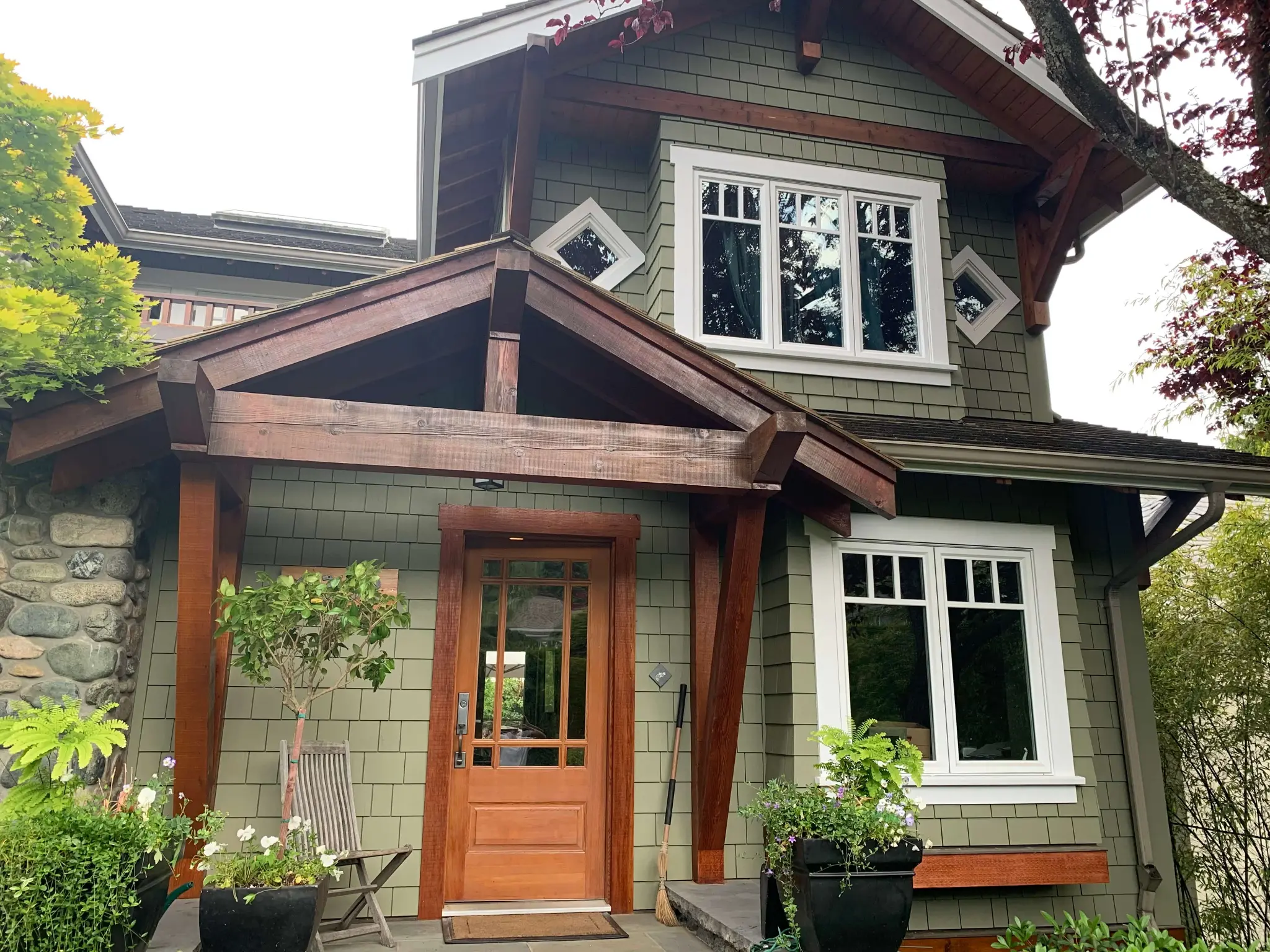 Completed exterior stain restoration at a large North Vancouver home with green siding, white trim, and natural wood details