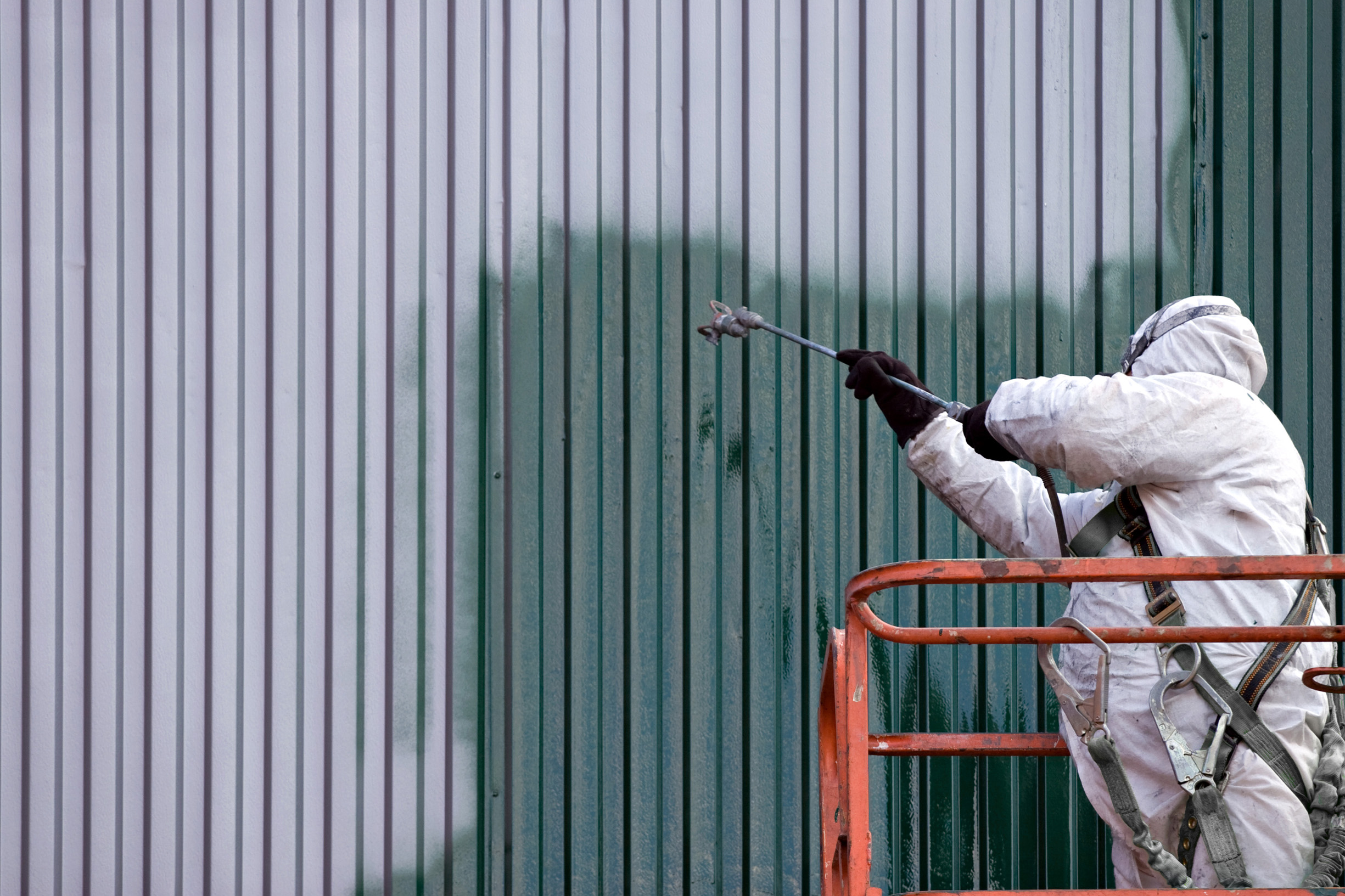 Commercial Building Exterior Spray Painting Painter in protective gear spray painting a green corrugated metal building.