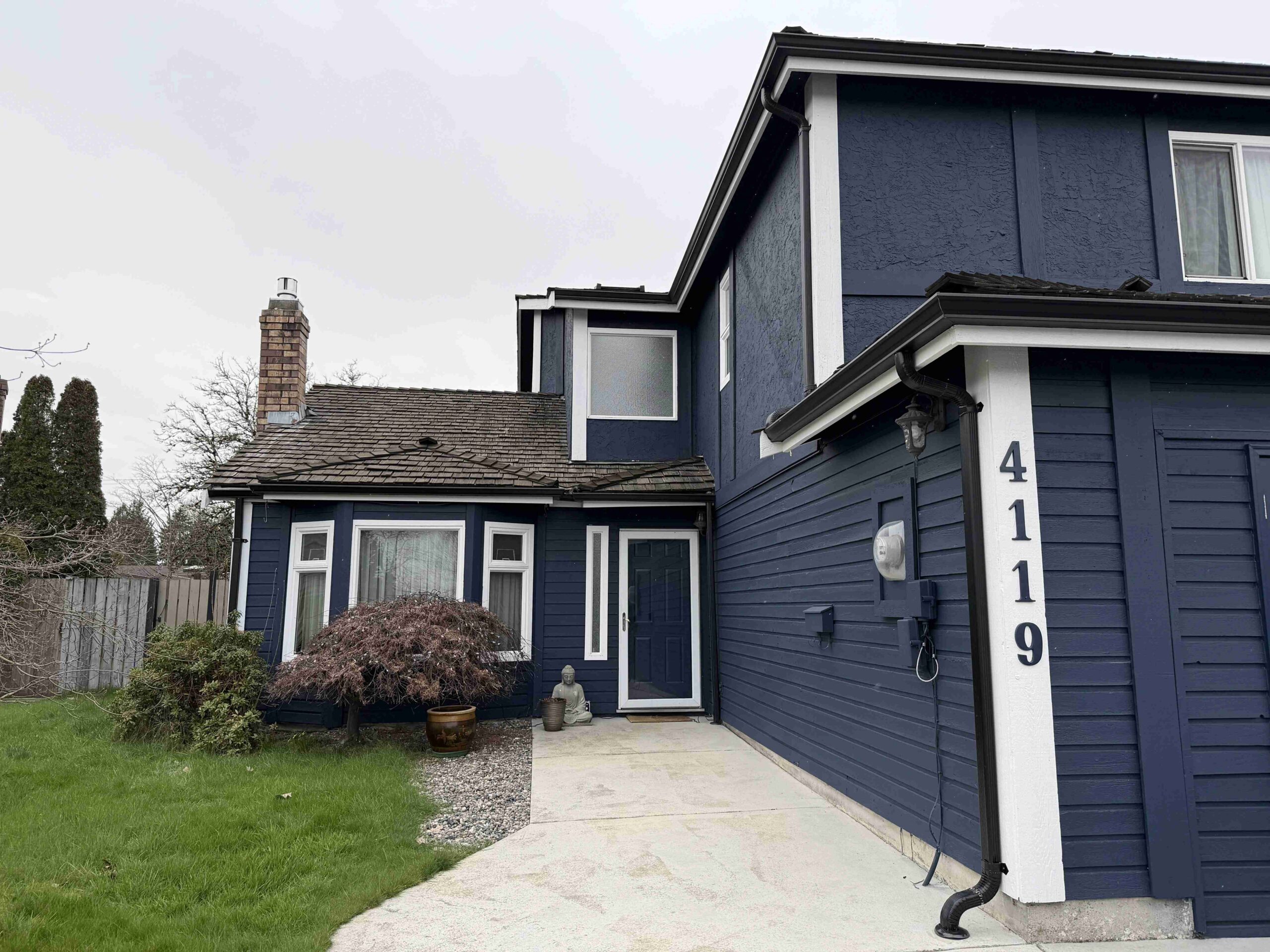 A freshly painted navy blue two story house with white trim and a concrete driveway, highlighting professional exterior painting.