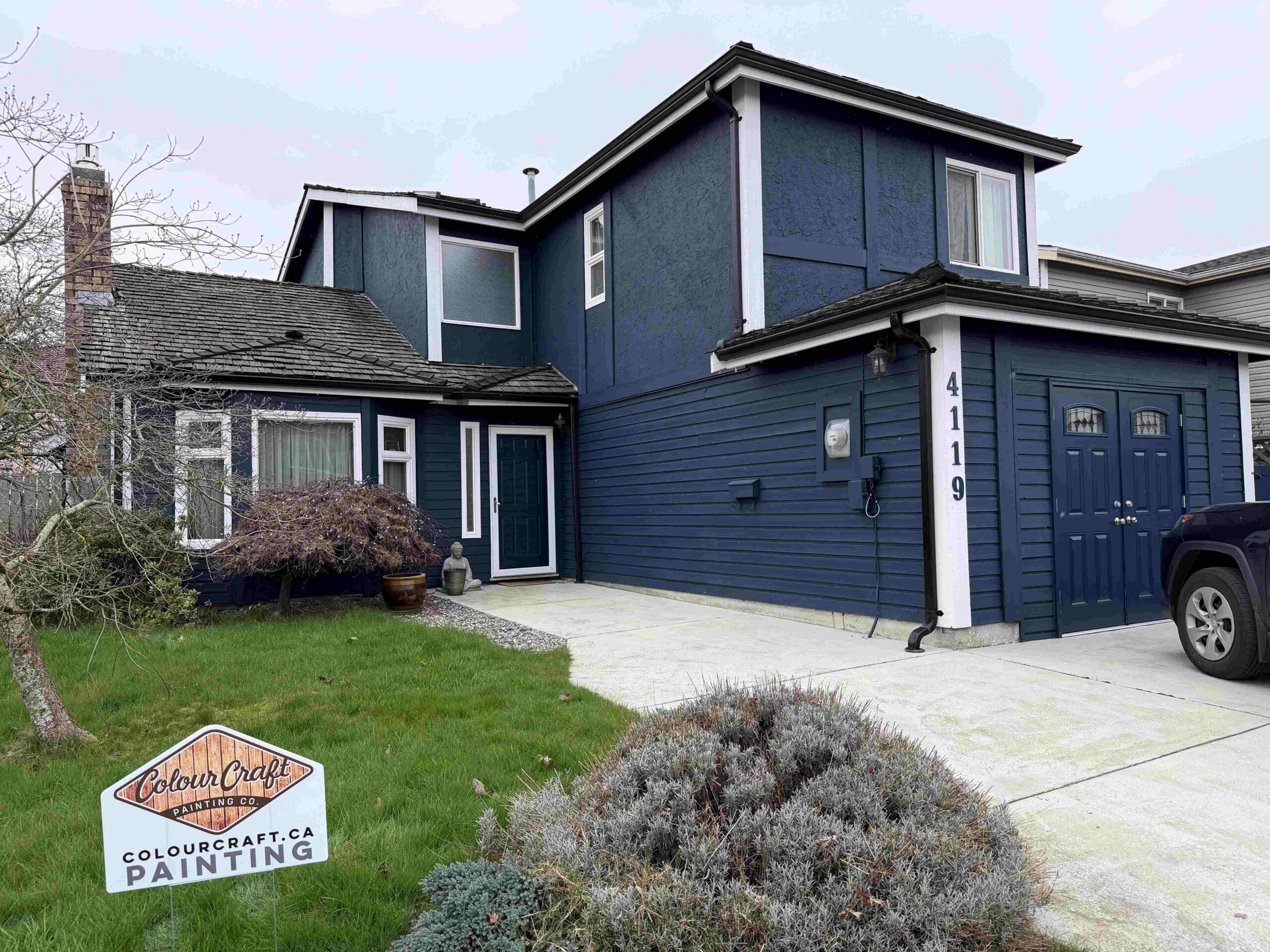 A freshly painted navy blue house exterior featuring white trim, a garage, and a Colour Craft Painting Co. sign.